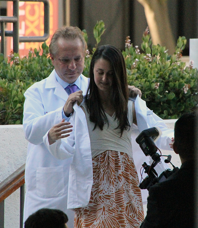 Dean Carmen A. Puliafito helps student physician Roxane Fries don her white coat.