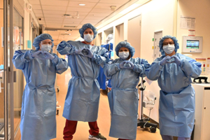 Four clinicians in full PPE make heart shapes with their hands.