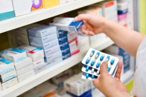 A pharmacist's hand takes a box from a shelf of medications.