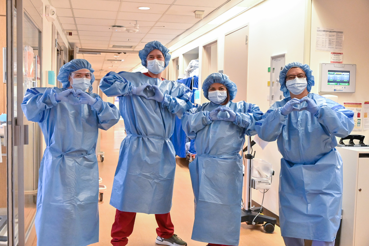 Four people in PPE make heart shapes with their hands