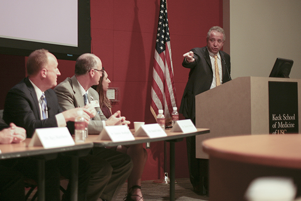 Keck School of Medicine of USC Dean Carmen A. Puliafito gestures to panelists Andrew A. Moshfeghi, Daniel Oakes and Sharon Orrange at a USC Alumni Board of Governors meeting.