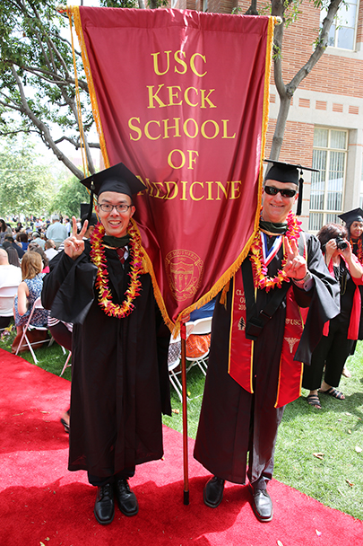 Velen Tat and Richard Bruce pose with the Keck School of Medicine of USC banner before the Primary Care Physician Assistant Program satellite commencement ceremony May 13, 2016 on the University Park Campus.