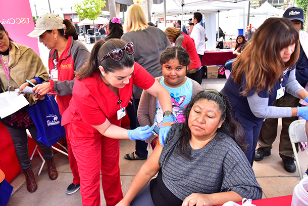Keck Medicine of USC Nurse Maria Saballos, in red scrubs, and Carmen Arlene Lizarraga, LVN, in blue scrubs, administer flu shots during the 26th annual Mariachi Festival, held Nov. 20 in Boyle Heights.