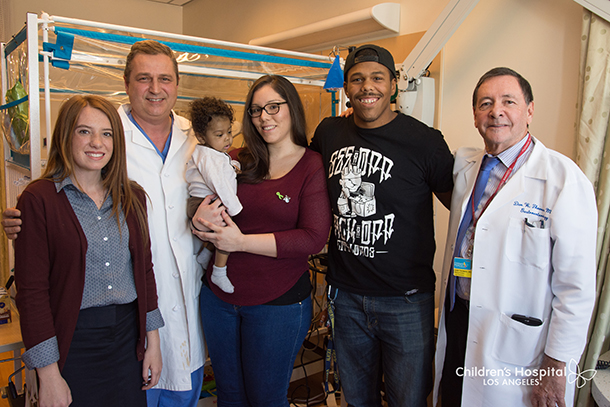Baby Donovan Daniels and his parents post-transplant in 2016, joined by doctors and, at left, Lydia Hand, now 18.