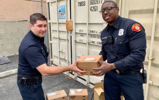 One uniformed man hands a sealed cardboard box to another.