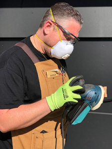 A man in a mask and goggles polishes a piece of protective equipment.