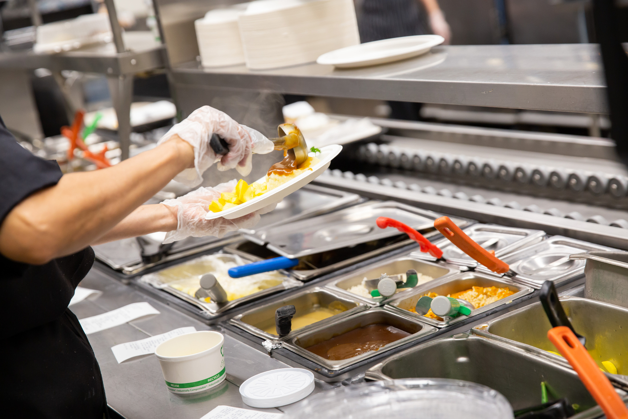 A food services worker dishes food onto a plate in a cafeteria setting
