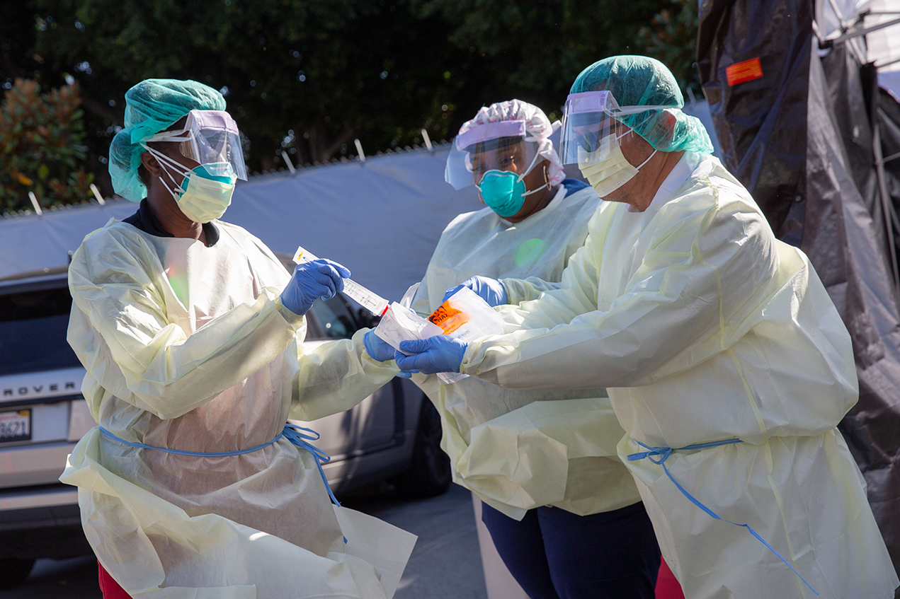 Three clinicians in full PPE process a swab test.