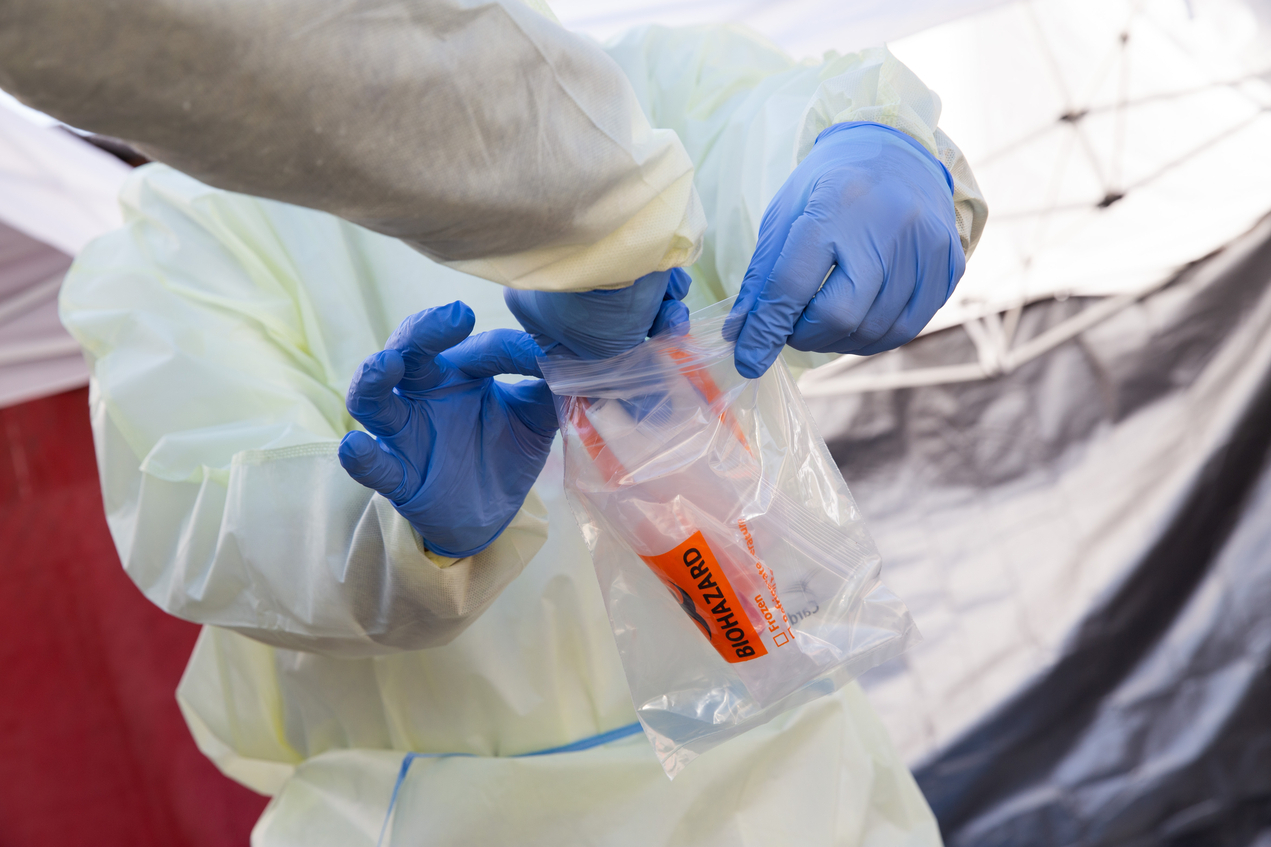 Gloved hands put a specimen marked biohazard in a plastic zippered bag
