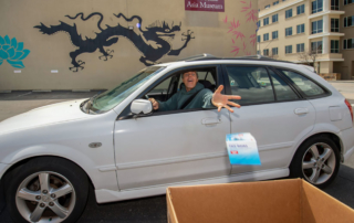 A man in a car tosses a small package into an open box.