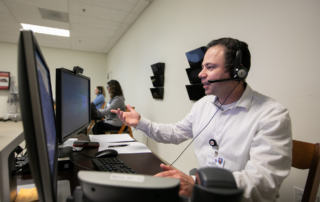 In a command center, a man talks on a headset and faces a monitor.