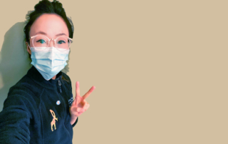 A young clinician in a mask flashes a peace sign.