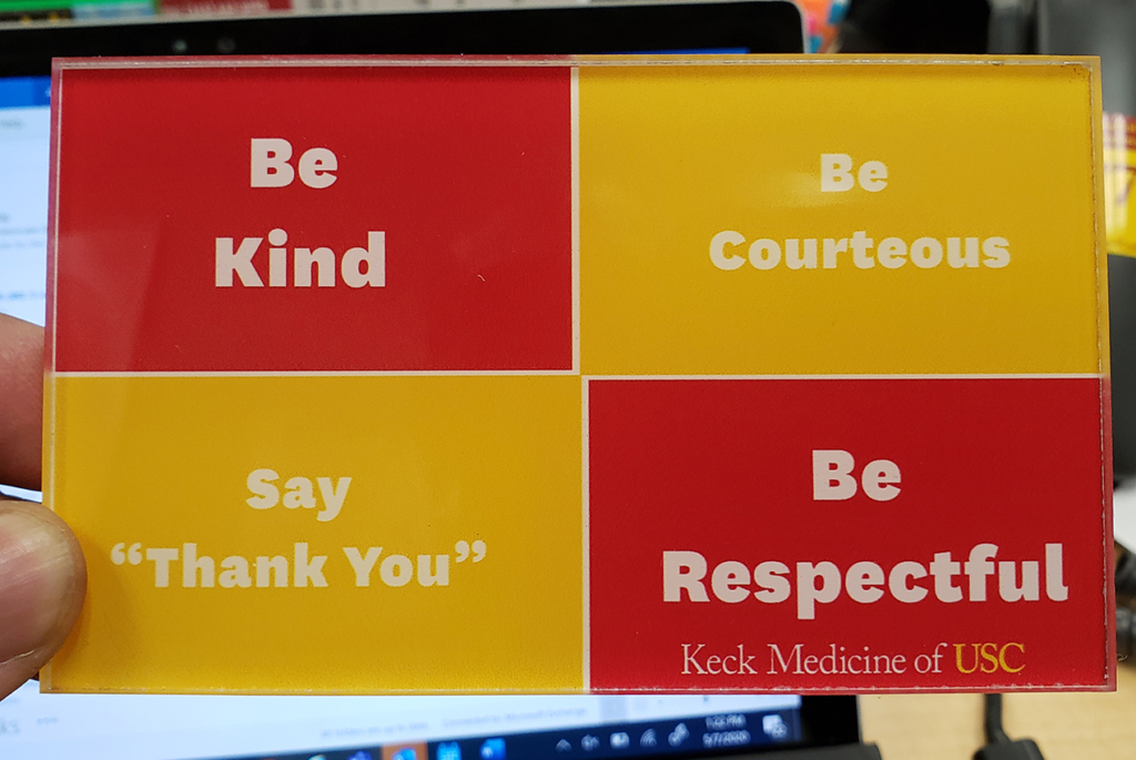 A hand holds a desk plate reminding people to be kind and courteous.