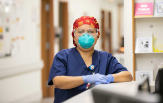 A woman in full PPE stands at a nurses' station.