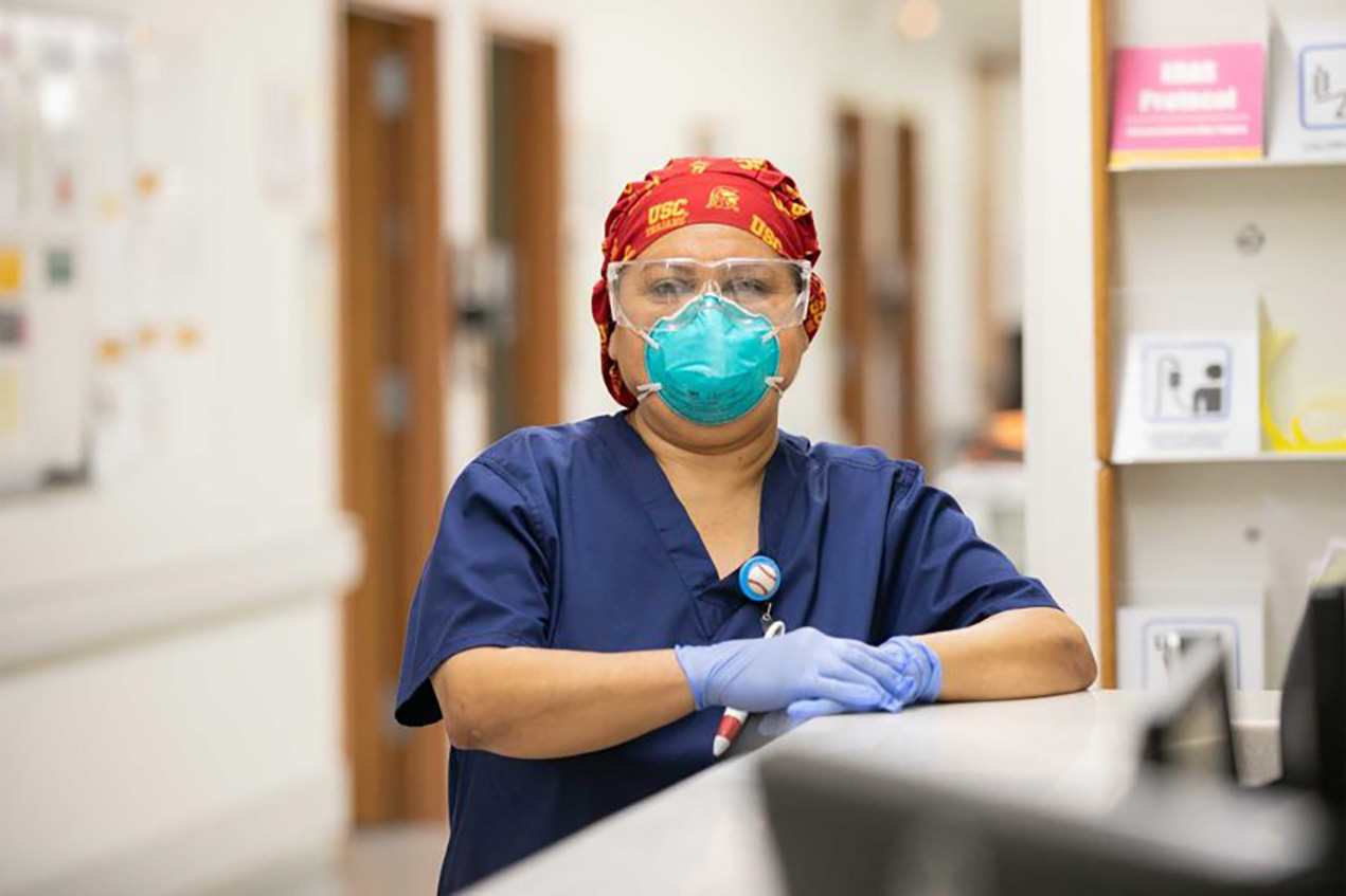 A woman in PPE stands at a nurses' station.