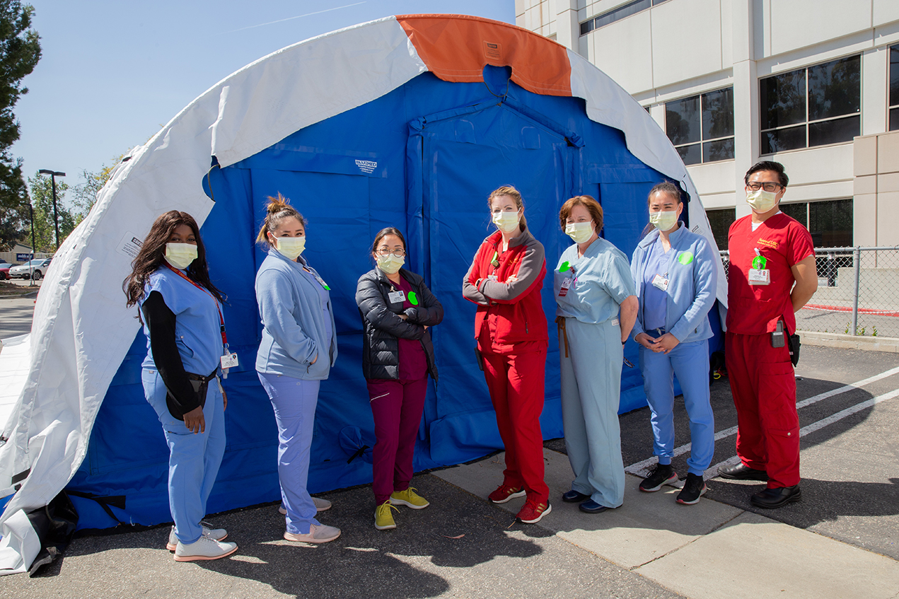 Seven masked health care professionals stand in front of a tent.