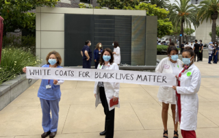 Women hold a banner reading White Coats for Black Lives Matter