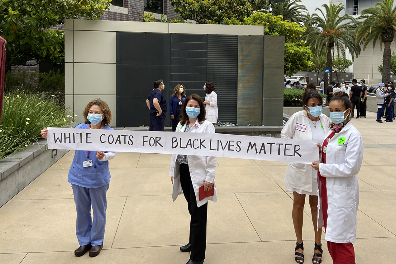 Four medical professionals present a banner reading White Coats for Black Lives Matter.