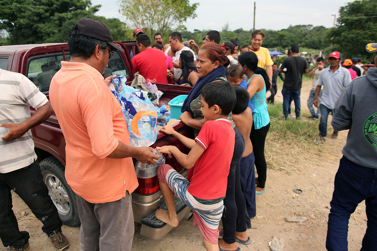 Asylum seekers gather around a pickup truck stocked with supplies.