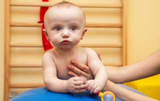Adult hands support a baby on an exercise ball.