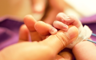 A woman's hand holds the hand of a tiny infant.