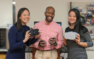 Three young adults beam as they hold virtual reality equipment.