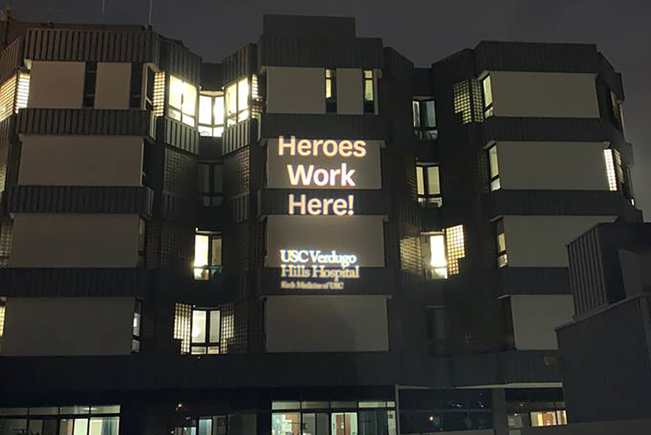 A projection on the side of a building reads, Heroes work here! USC Verdugo Hills Hospital, Keck Medicine of USC.