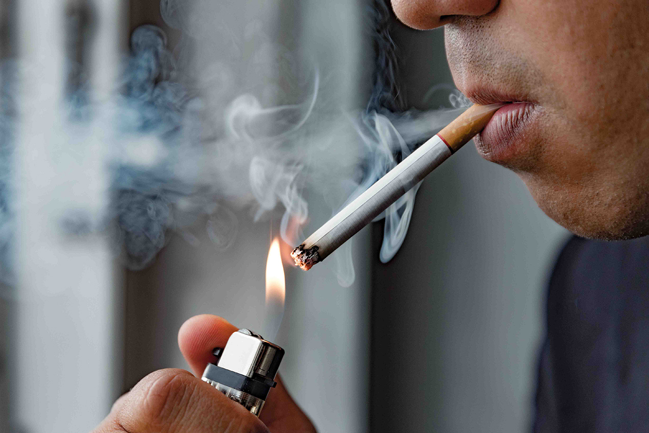 A closeup shows a young man lighting a cigarette.