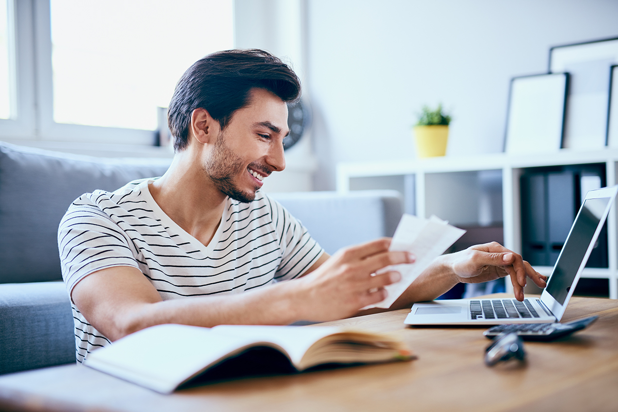A smiling man looks at papers and a laptop