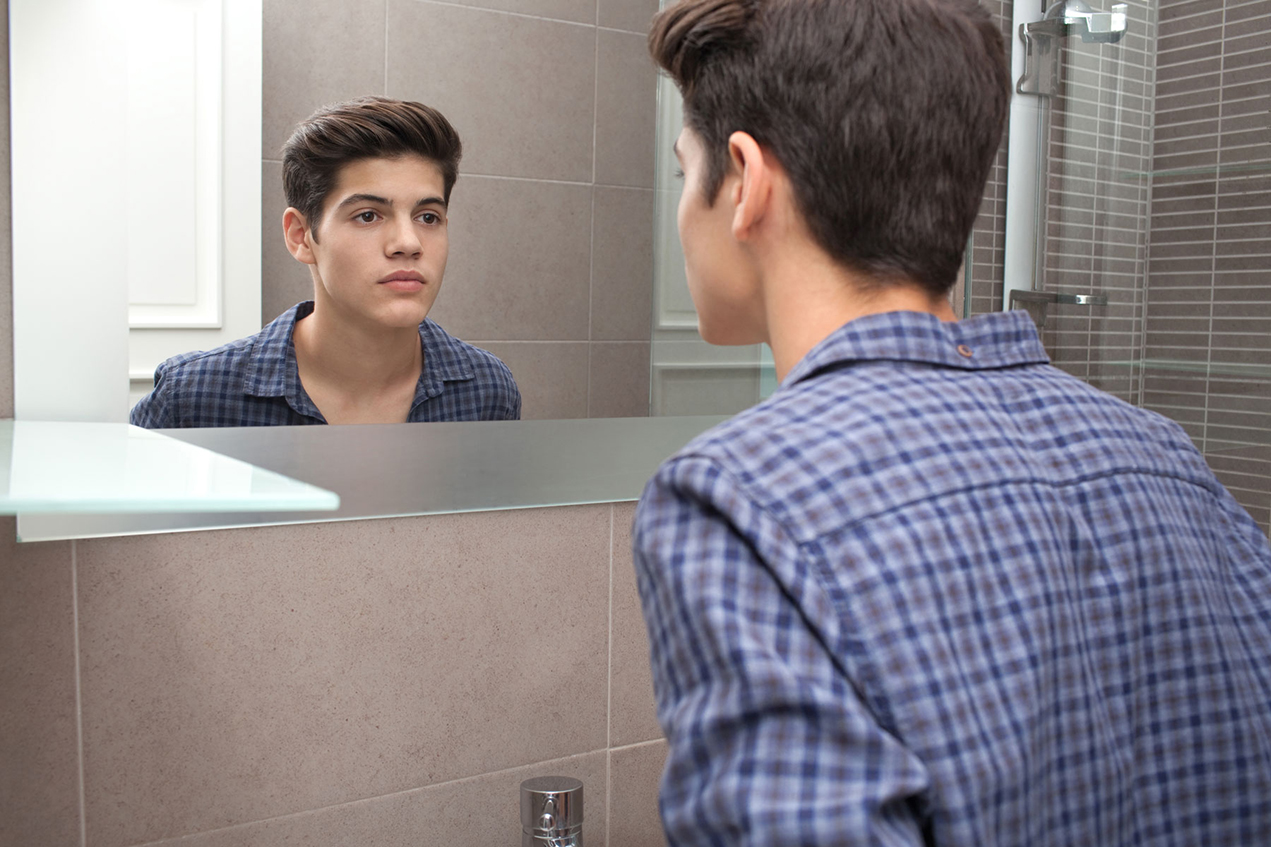 A young man looks at his reflection in a bathroom mirror
