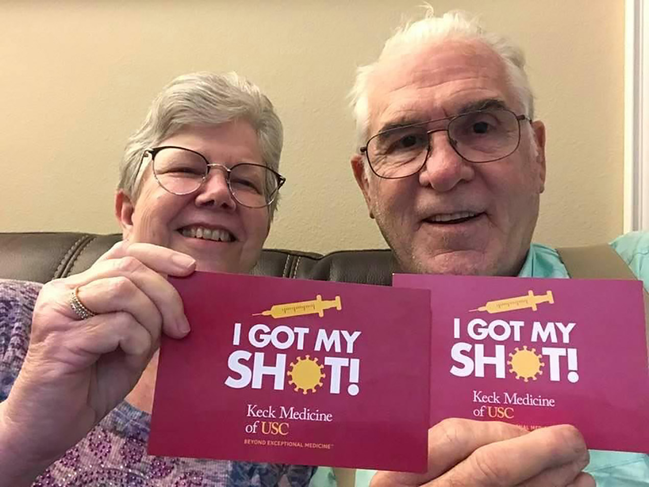 A smiling older couple holds up postcards that say I Got My Shot