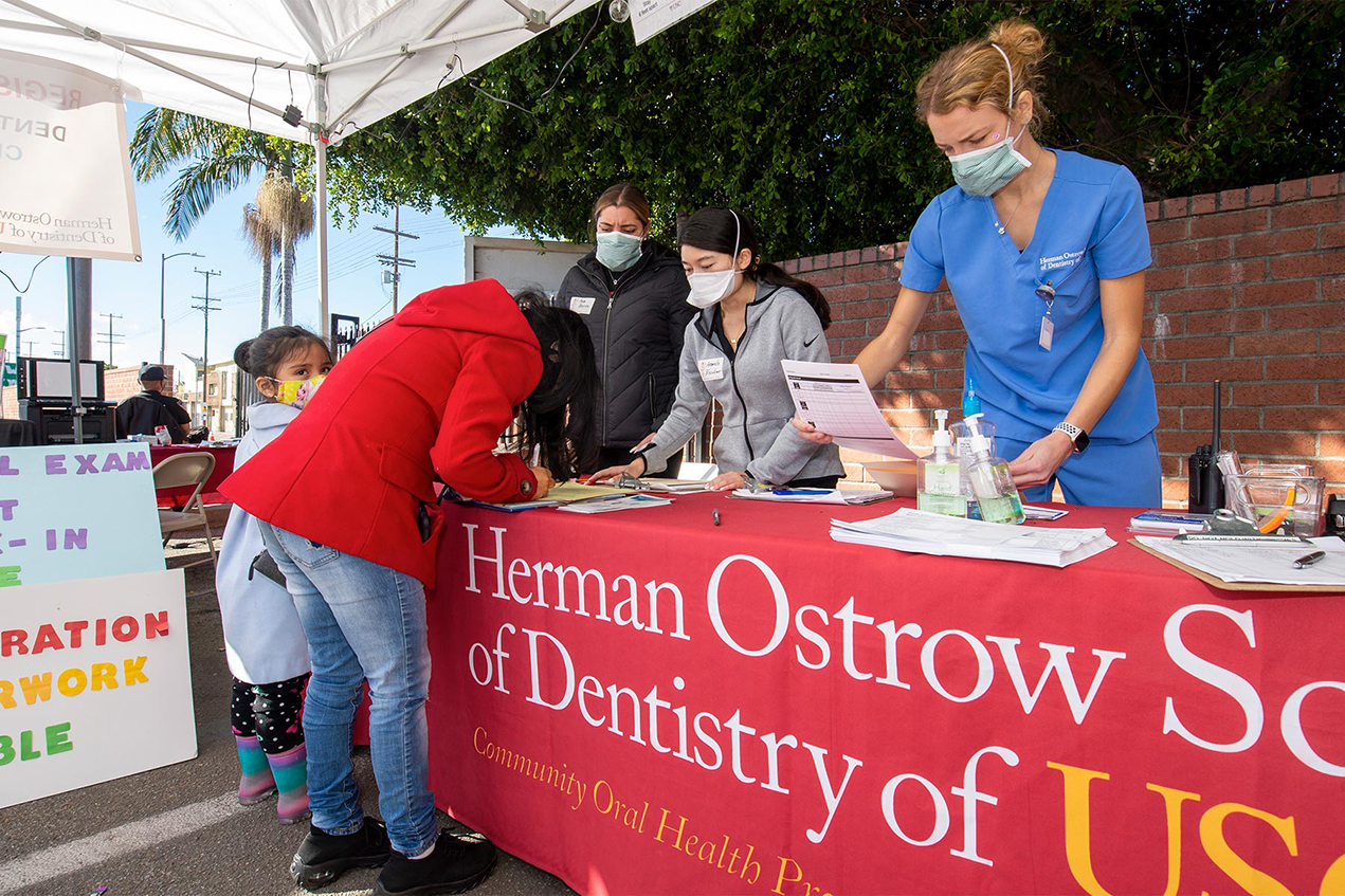 Jaqueline Solorio, 4, looks on as mother Vanessa Velasquez checks in with [left to right] USC dental administrative assistant Ana Parru, dental student Amanda Escobar and dental surgery student Abigail Heleba as part of the monthlong mobile dental clinic event in South Los Angeles.