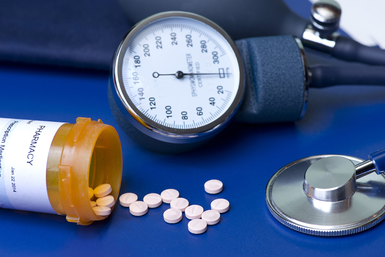 A blood pressure gauge, stethescope and a spilled pill bottle are seen on a blue background