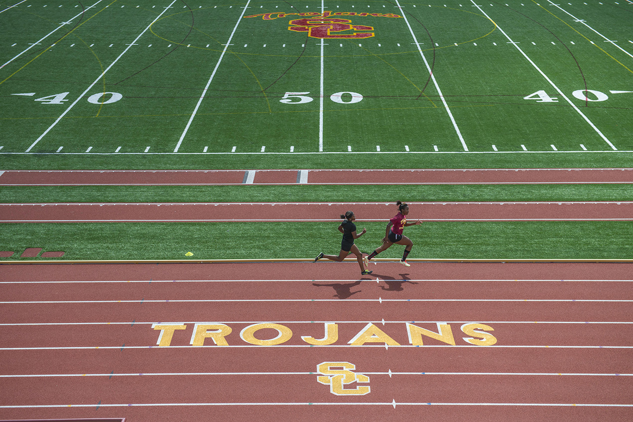 Two people are seen running on a track above the Trojans SC logo