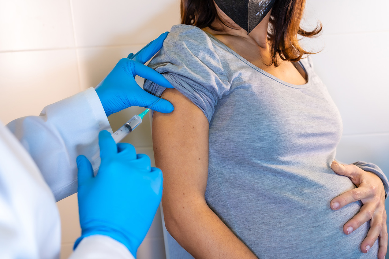A pregnant woman touches her belly while a person wearing gloves pushes up her sleeve and holds a syringe