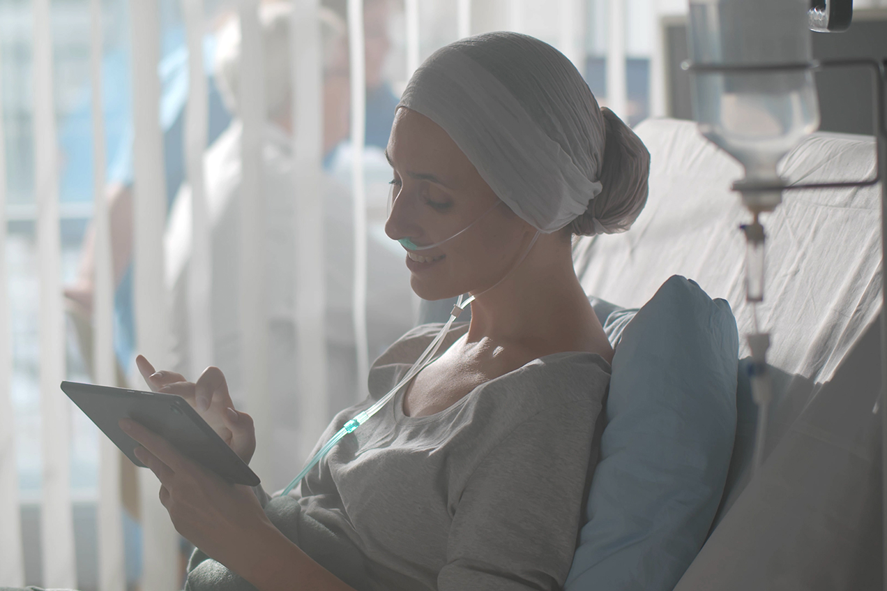 A hospitalized cancer patient smiles as she uses a tablet