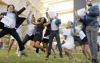 A group of students holding certificates jump in the air.