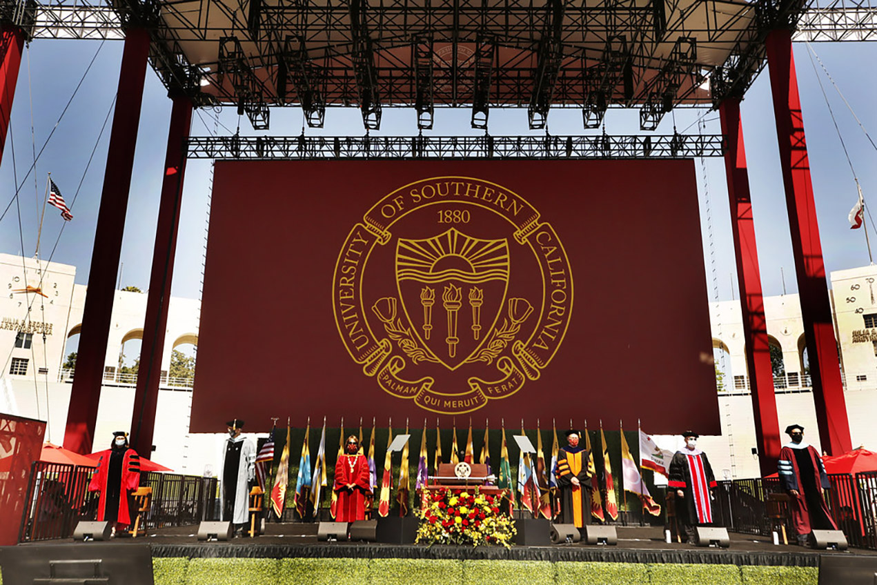 A stately commencement stage features a backdrop bearing the USC seal