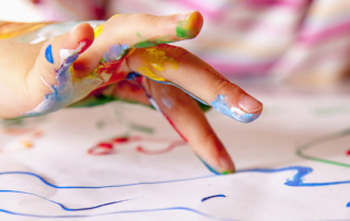 A closeup shows a child's hand fingerpainting.