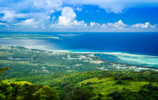An aerial view shows a gorgeous, tropical island beneath a blue sky.