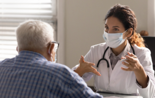 A masked doctor gives an older male patient an explanation.
