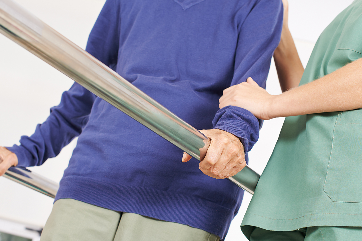 A woman in scrubs helps an older patient practice walking