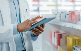 A pharmacist uses a tablet by a shelf of supplies.