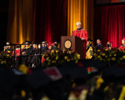 A man with bleached, spiky hair speaks at a commencement ceremony