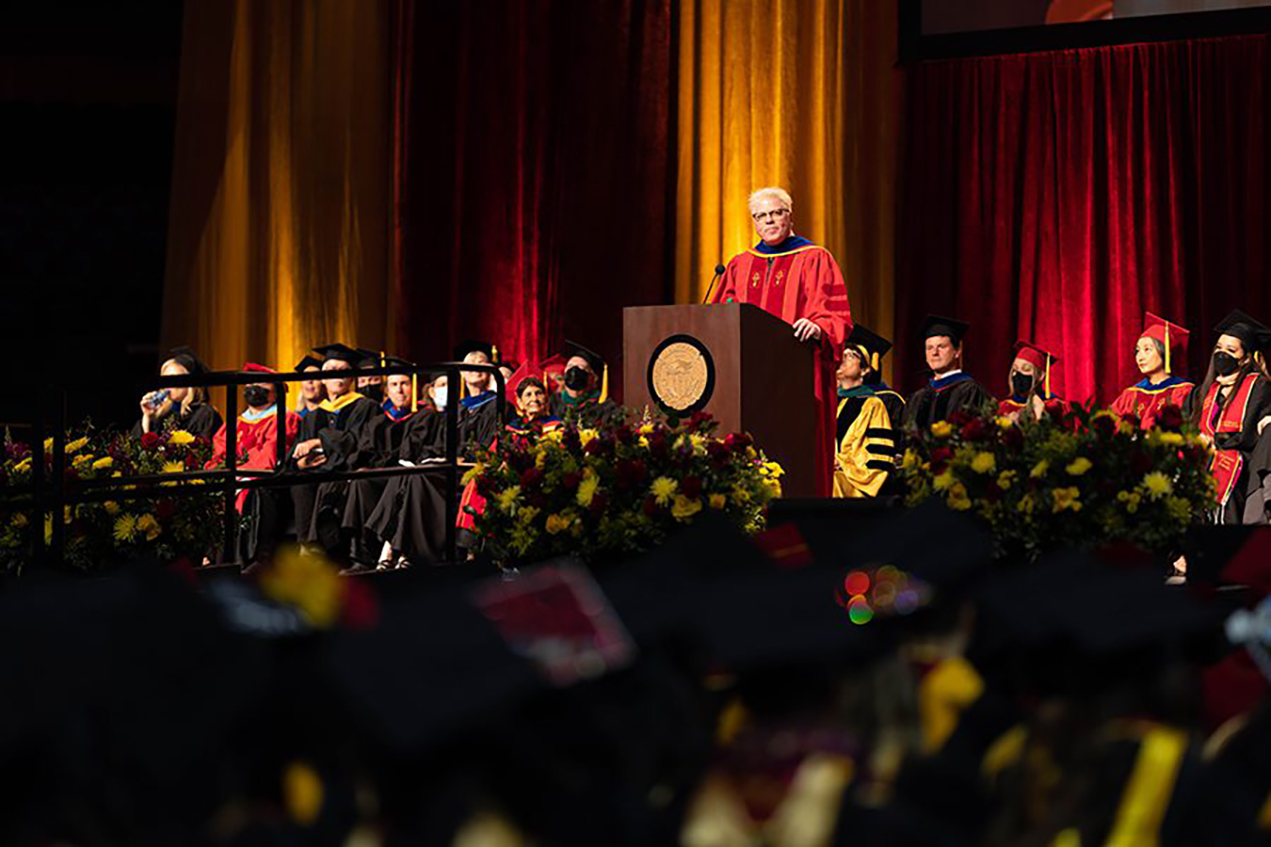 A man with bleached, spiky hair addresses a room full of graduates