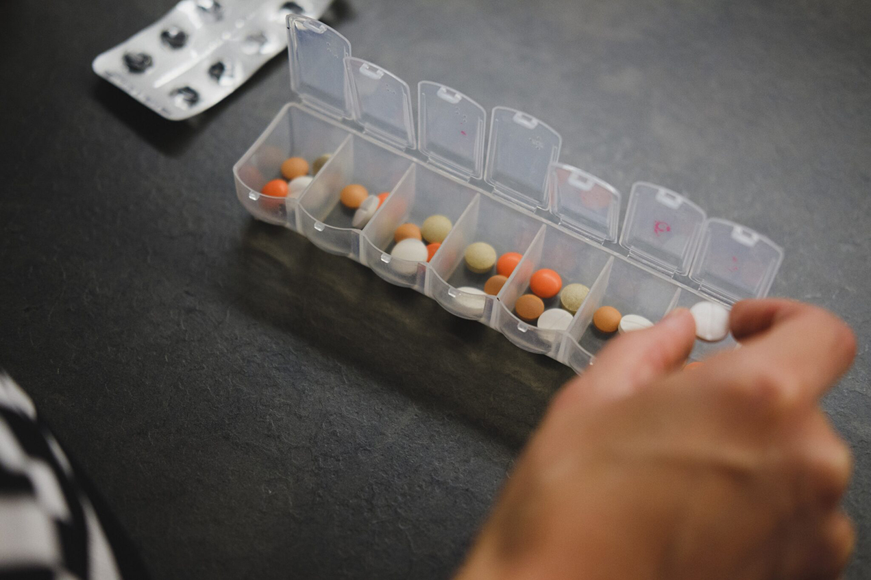 A hand places tablets in a daily pill sorter