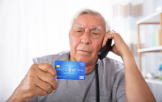 An older man holds a credit card as he uses a phone.