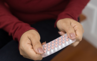 A closeup shows a woman's hands holding a pack of oral contraception