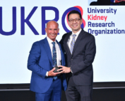 A bald man smiles as he accepts an award from a bespectacled man