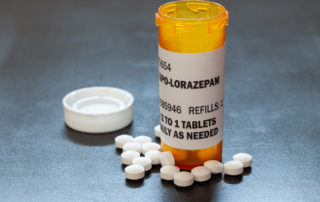 Several pills lie around the base of an open prescription pill bottle.